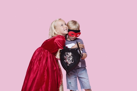 Happy young girl in princess costume hugging boy pretending to be her hero over pink backgroundの写真素材
