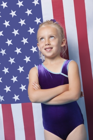 Happy young female gymnast with arms crossed standing in front of American flagの写真素材