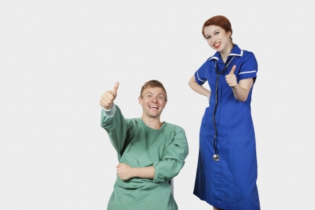 Portrait of young male patient with female nurse gesturing thumbs up against gray backgroundの写真素材