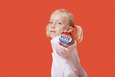 Portrait of a young girl showing vote badge over pink backgroundの写真素材