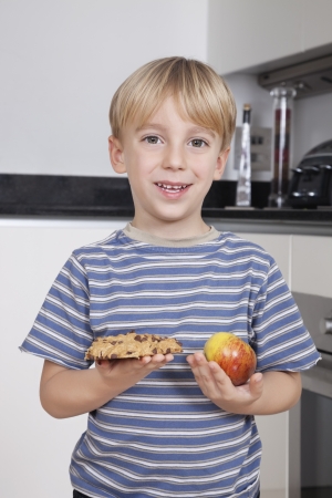 Portrait of cute little boy choosing between apple and chocolate chip cookieの写真素材