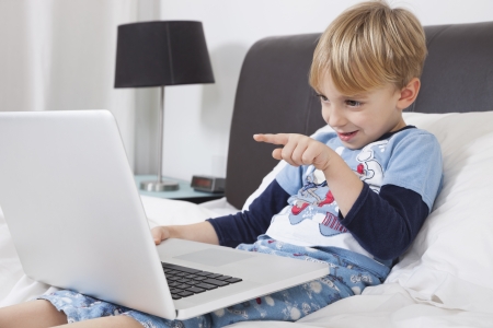 Playful Caucasian boy using laptop computer in bedの写真素材