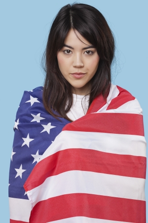 Patriotic young woman wrapped in American flag over blue backgroundの写真素材