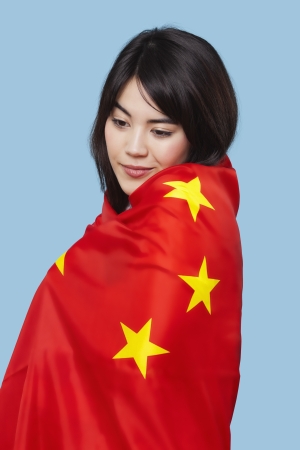 Patriotic young woman wrapped in Chinese flag over blue backgroundの写真素材