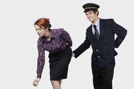 Portrait of young pilot touching flight attendant inappropriately against gray backgroundの写真素材