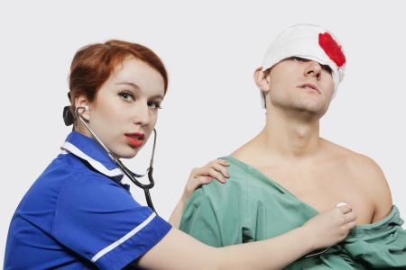 Portrait of female nurse treating an injured male patient against gray backgroundの写真素材