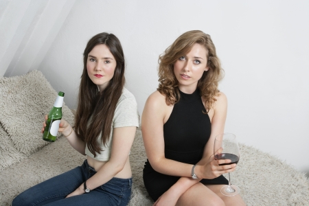 Portrait of two young women having drinks while sitting on sofaの写真素材