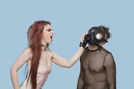 Funky young woman slapping man in gas mask over blue backgroundの写真素材