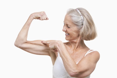 Senior woman flexing muscles against white backgroundの写真素材