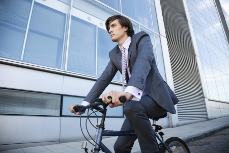 Low angle view of young businessman riding bicycle by buildingの写真素材