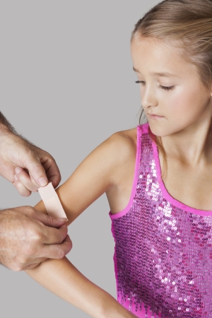 Hands applying adhesive bandage on girl's arm against gray backgroundの写真素材