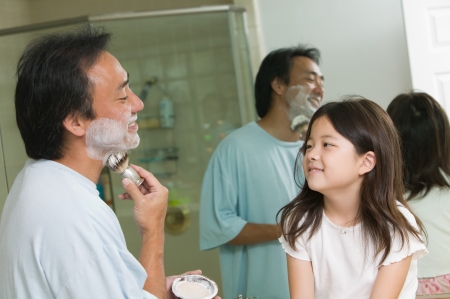 Daughter watching father apply shaving cream in bathroomの写真素材