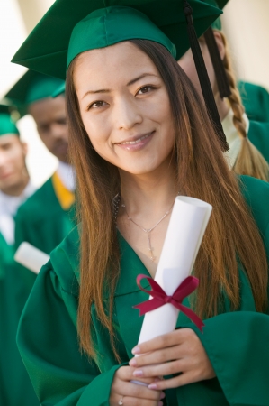 Graduate Holding Diploma outside with others behind portraitの写真素材