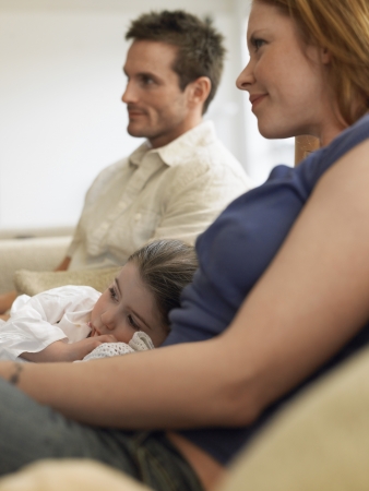 Girl (3-4) watching television with parents on couchの写真素材