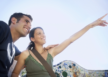 Young couple sitting on stone bench woman pointing into distance portraitの写真素材