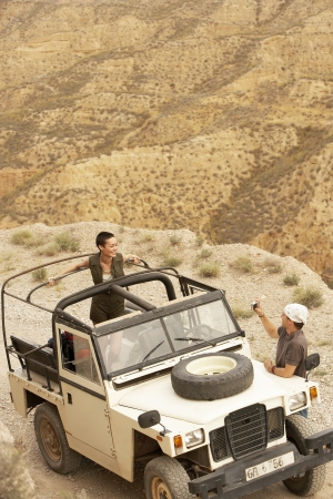 Man photographing woman standing in four wheel drive car on edge of cliff elevated viewの写真素材