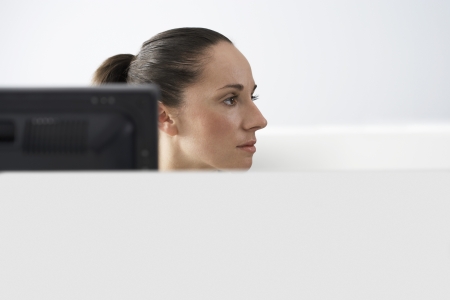 Female office worker sitting behind monitor in office cubicle portraitの写真素材