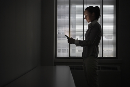 Female office worker standing using mobile phone in darkened office side viewの写真素材