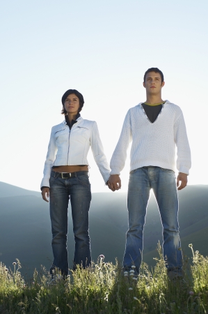 Young couple standing in mountain field looking at view, front view, low angle viewの写真素材