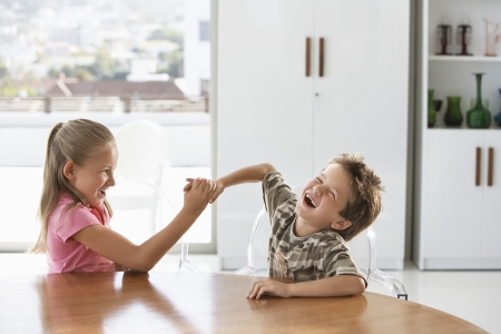 Young girl and boy fighting at table at homeの写真素材