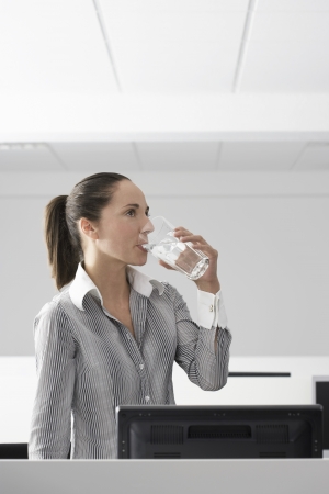 Female office worker drinking water in office cubicleの写真素材
