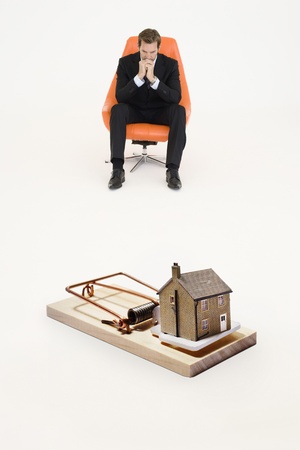 Model home on mouse trap with worried businessman sitting on chair representing increasing real estate ratesの写真素材