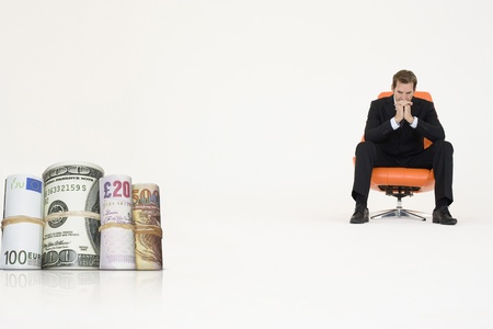 Money rolls with pensive businessman on chair representing financial problemsの写真素材