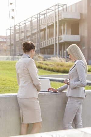 Young businesswomen working together on laptop while standing against office buildingの写真素材