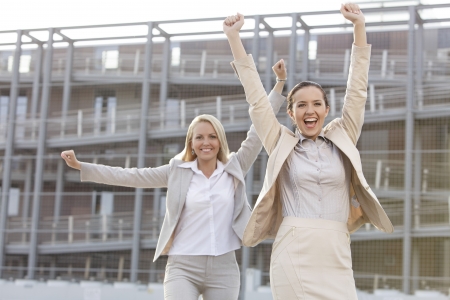 Excited young businesswomen with arms raised against office buildingの写真素材