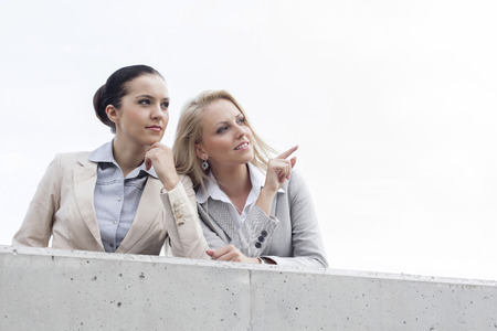 Low angle view of happy young businesswoman showing something to coworker while standing on terrace against skyの写真素材