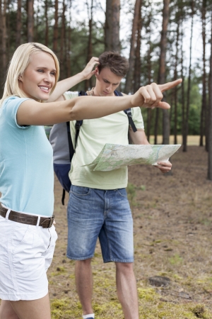 Young woman pointing away with confused man holding map in forestの写真素材