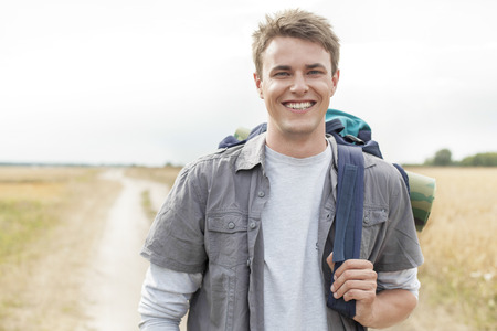 Portrait of happy male hiker with backpack standing on fieldの写真素材