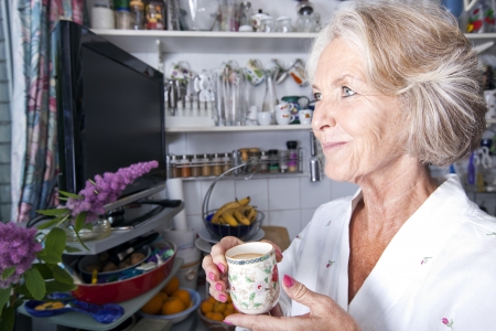 Thoughtful senior woman looking away while holding coffee cup in kitchenの写真素材