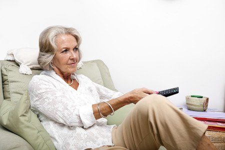 Senior woman using remote control while relaxing on armchair at homeの写真素材