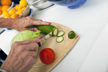 Cropped image of senior woman cutting vegetables on chopping board in kitchenの写真素材