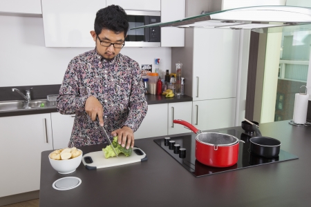 Young man chopping broccoli at kitchen counterの写真素材