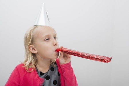 Little girl wearing party hat blowing noisemaker at homeの写真素材