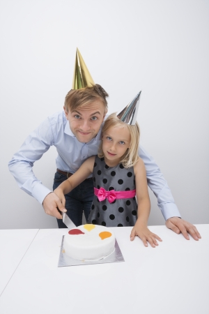 Portrait of father and daughter cutting birthday cake at tableの写真素材