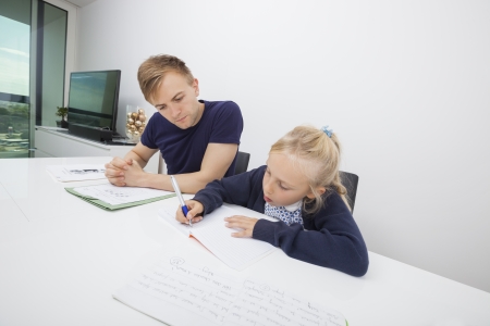 Little girl studying while sitting by father at tableの写真素材