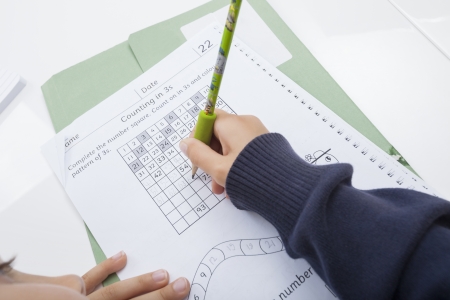 Close-up of girl's hand writing numbers on documentの写真素材
