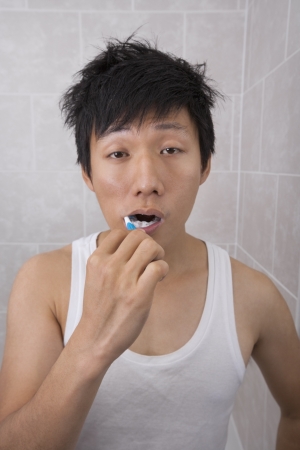 Sleepy mid adult man brushing teeth in bathroomの写真素材