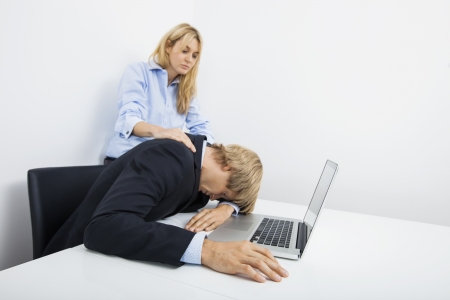 Businesswomen with overworked coworker at desk in officeの写真素材