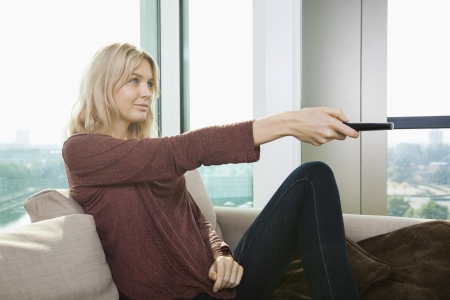Side view of young woman watching television on sofa at homeの写真素材