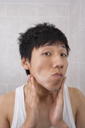Portrait of mid adult man applying aftershave lotion in bathroomの写真素材