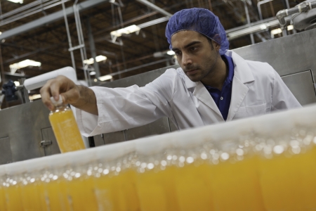 Mid adult industrial worker looking at bottle in factoryの写真素材