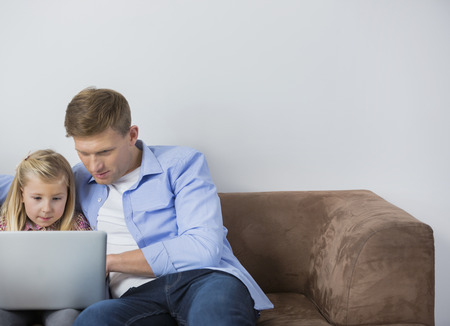Father and daughter using laptop together on sofa at homeの写真素材