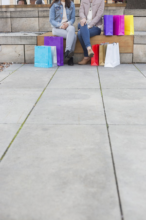 Low section of female friends with shopping bags sitting on steps with sidewalk on foregroundの写真素材