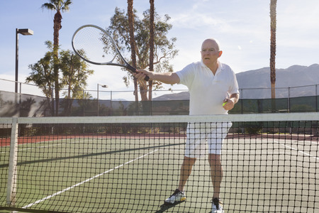 Senior male tennis player preparing to serve on courtの写真素材