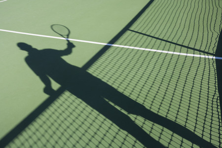 Shadow of senior man playing tennis on courtの写真素材