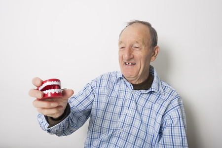Happy senior man holding dentures against gray background